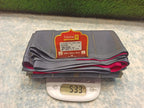 Stack of gray pants with a label on a digital scale showing weight, against a textured surface.