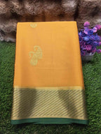 Yellow saree with gold border on a green surface with flowers in the background