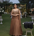 Woman in a brown evening gown standing outdoors with decorative lights and flowers in the background