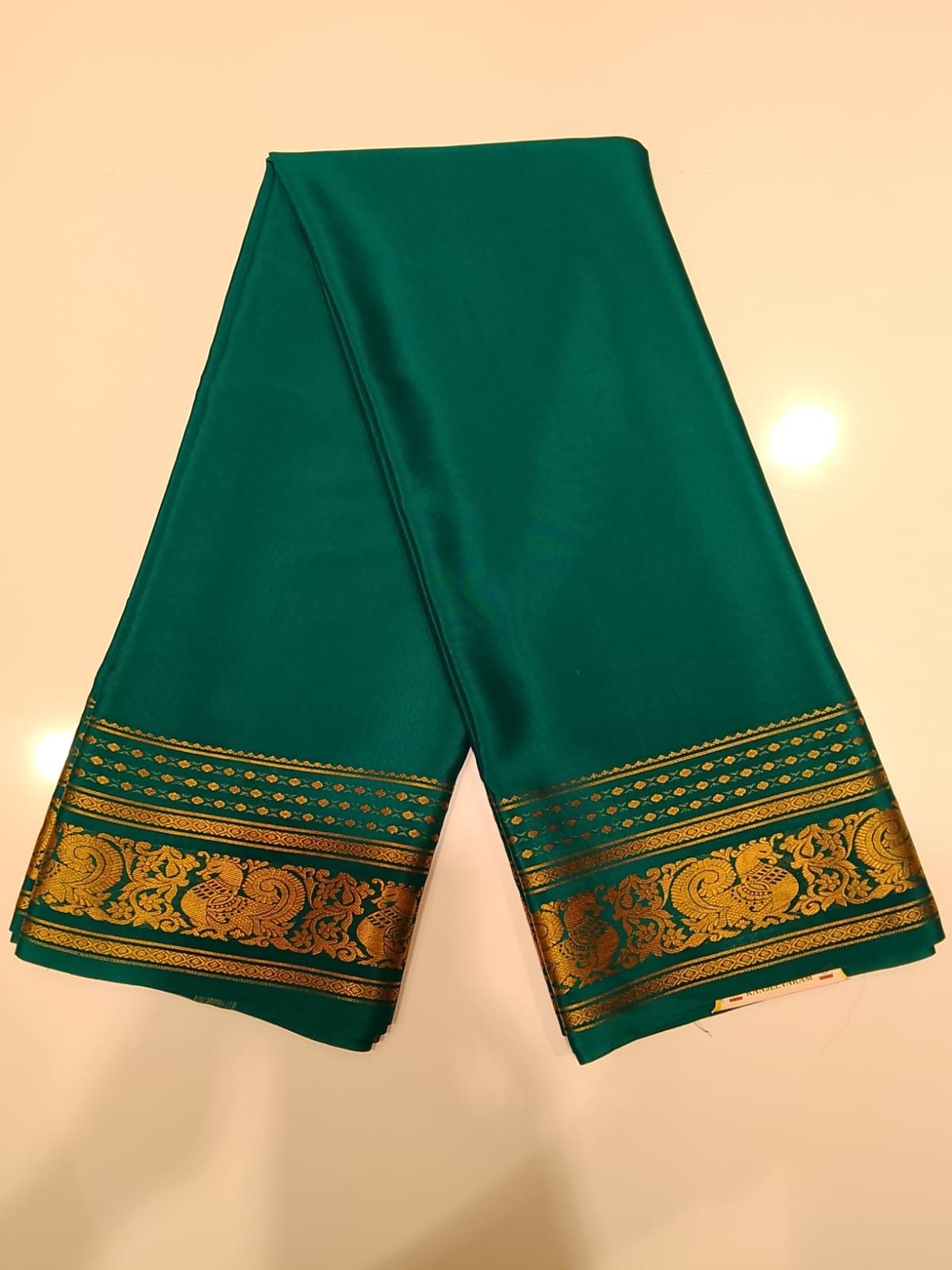 Teal Kanjivaram silk saree with gold zari peacock border, folded view